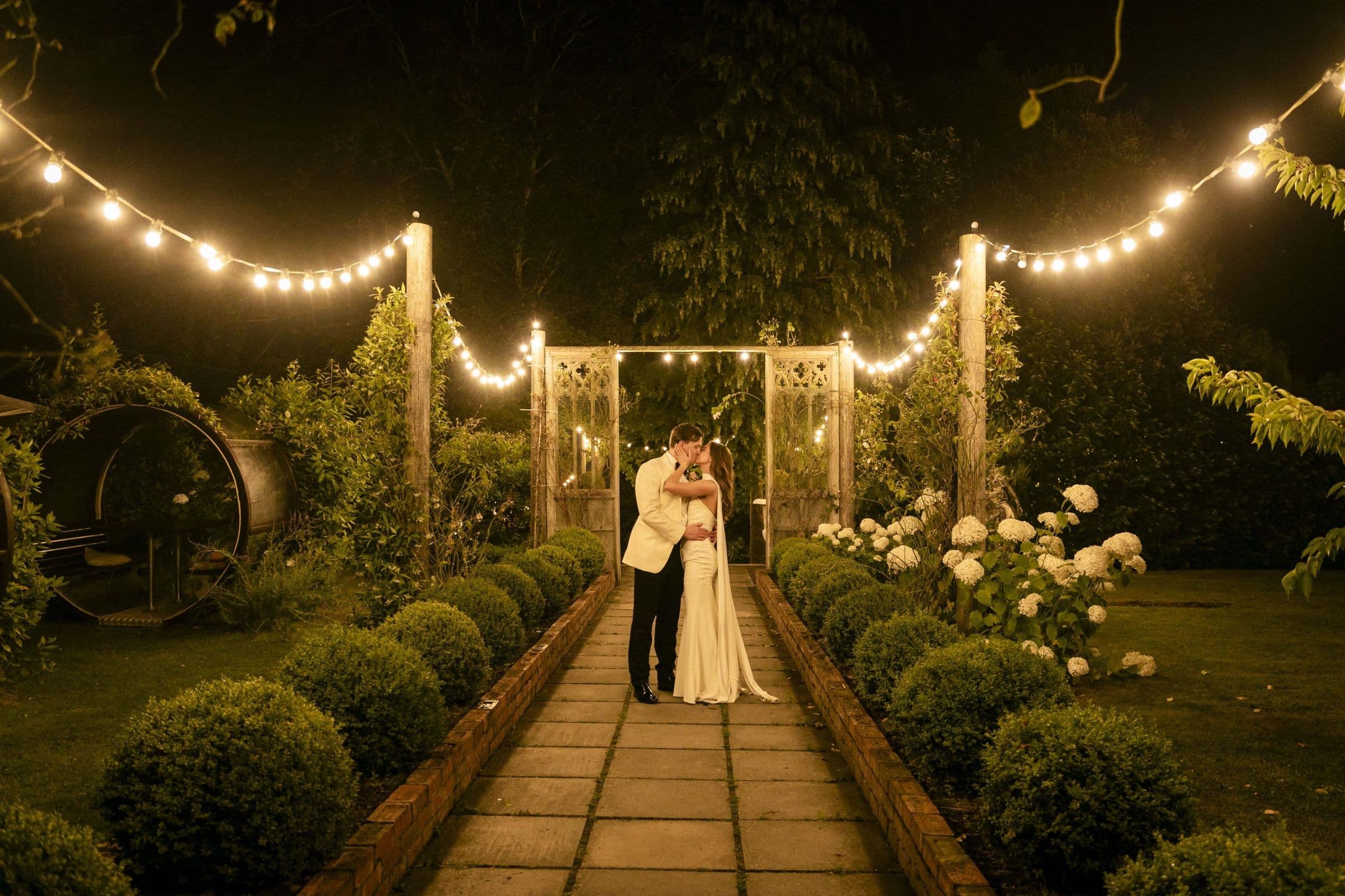 Bride and groom under festoon lights in a garden at night