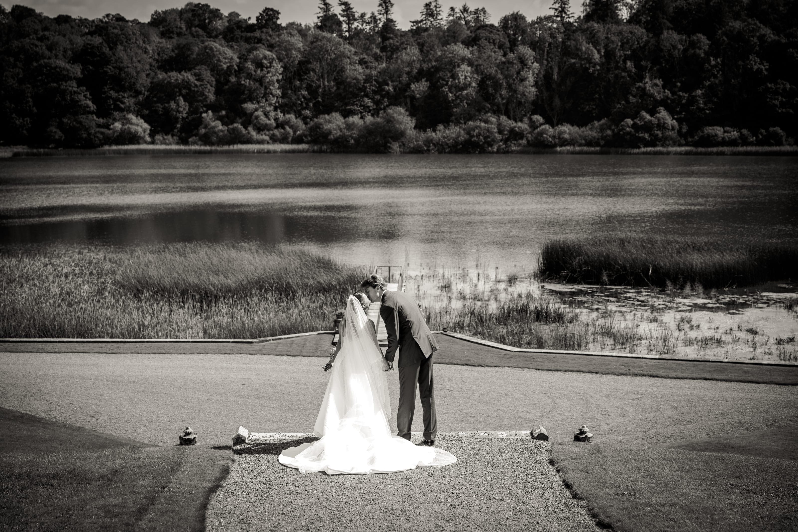 Bride and groom kissing on a terrace above a lake, in black and white