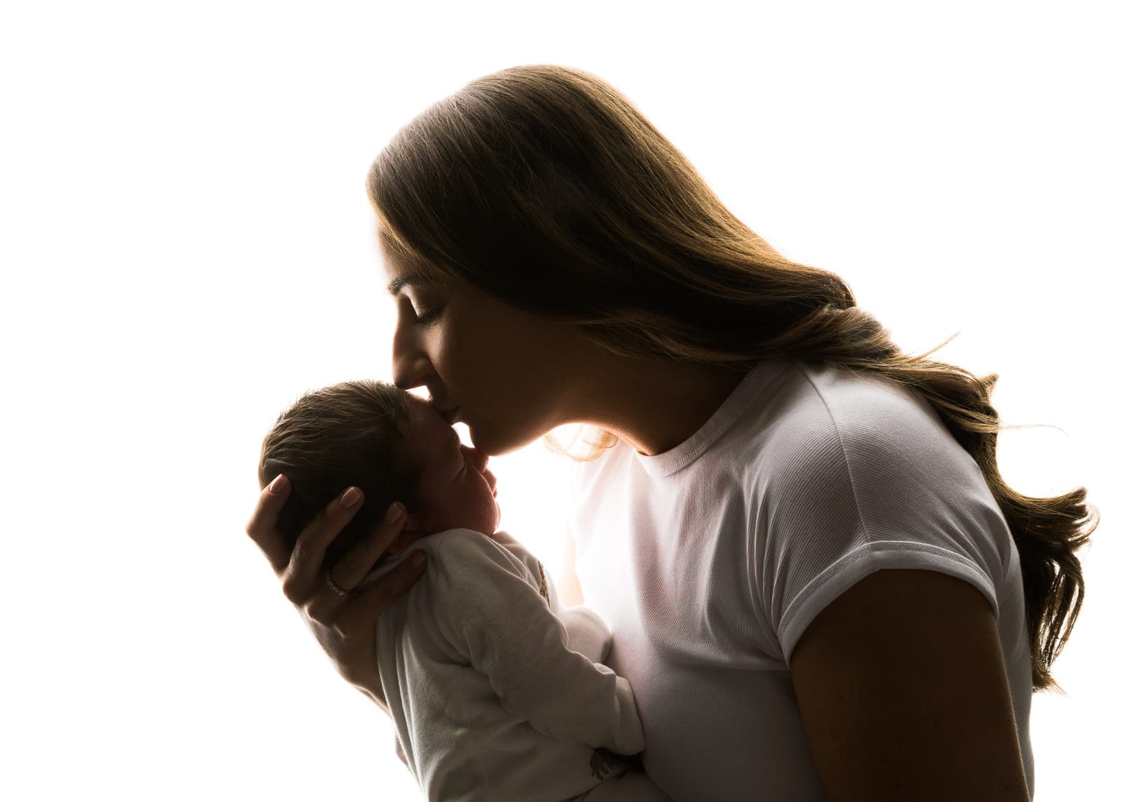 Mother kissing her newborn, in silhouette