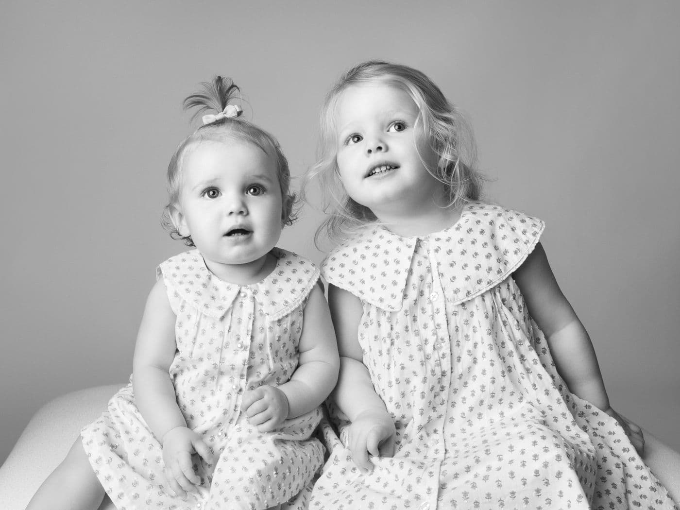 Two little girls in matching dresses with wide collars, both looking up, in black and white