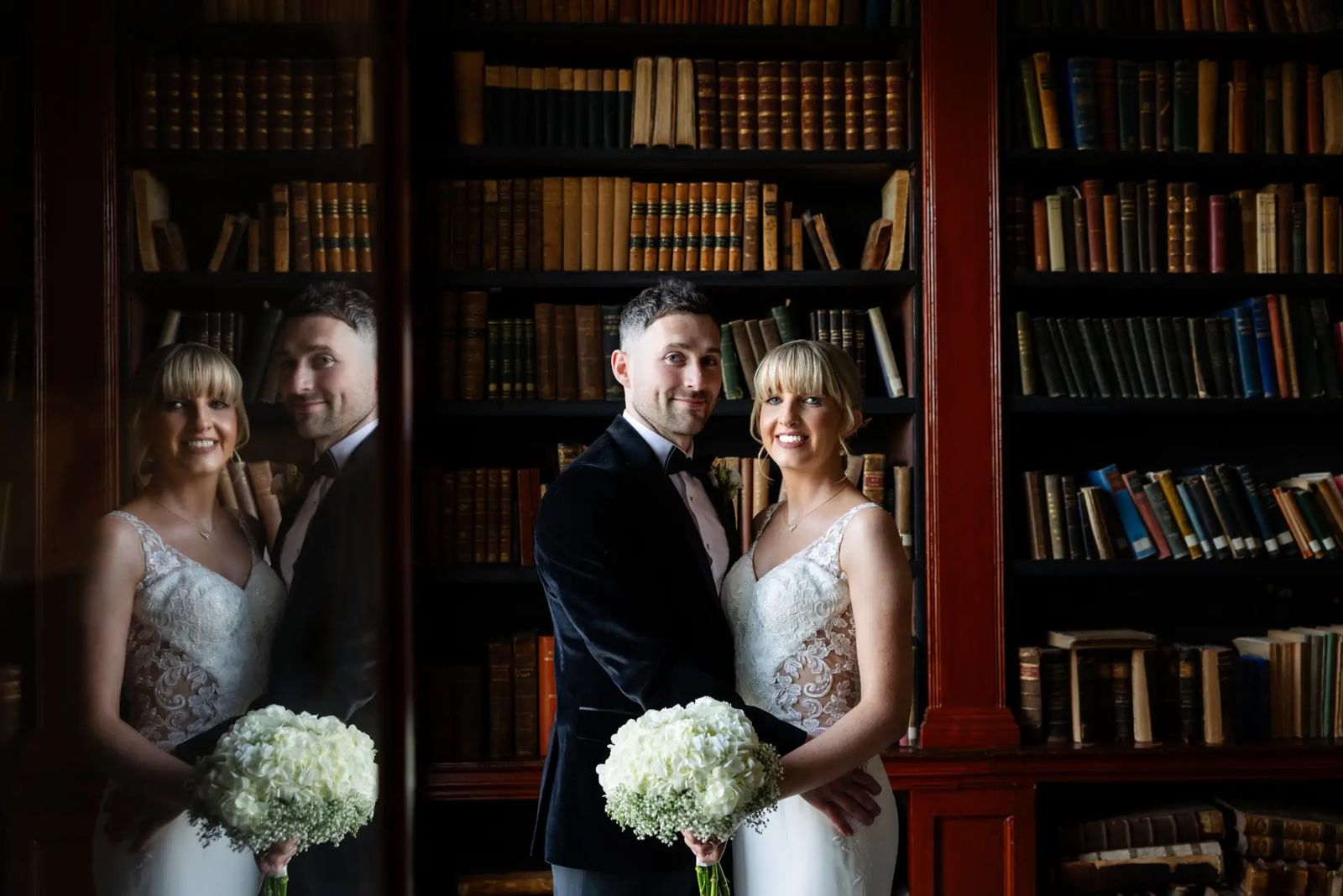 Bride and groom in a library of old books, reflected in a pane of glass beside them